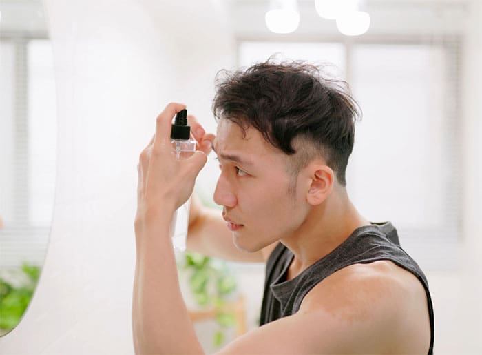 a male is styling his hair and looking into the mirror