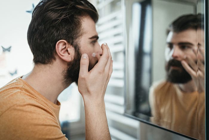 a male wearing yellow shirt looking into mirror and doing skin care