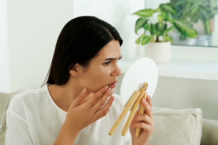 a female wearing white shirt looking into mirror and doing skin care