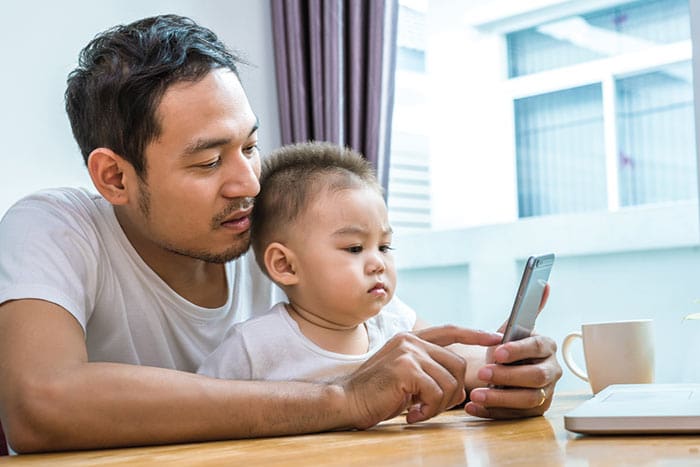 a male in white with his kid having a online Telehealth consultation from their home