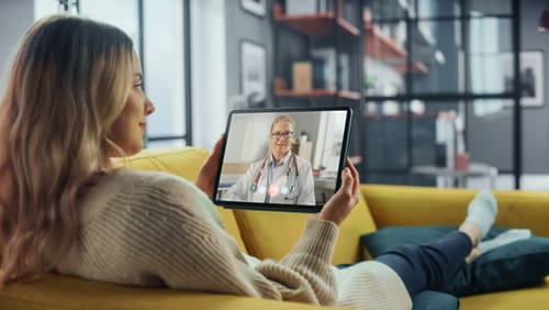 Girl in brown sweater having online Telehealth consultation with doctor on a yellow couch